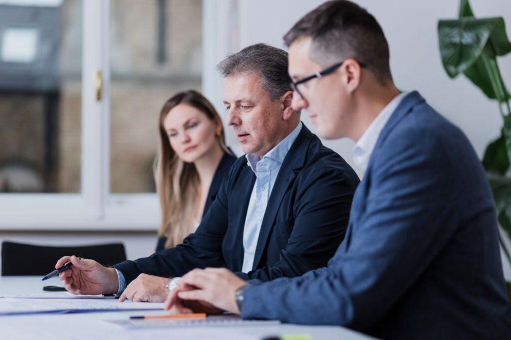 Drei Personen in einem Besprechungsraum, zwei Männer und eine Frau bei der Arbeit – Symbolbild für Teamarbeit und Karriere bei P&K Nord ZT-GmbH