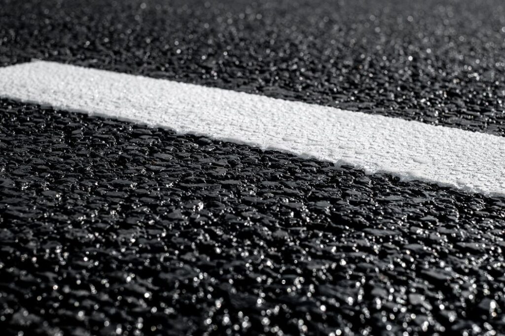 Makroaufnahme einer asphaltierten Fahrbahn mit weißer Straßenmarkierung – Symbolbild für Straßenplanung