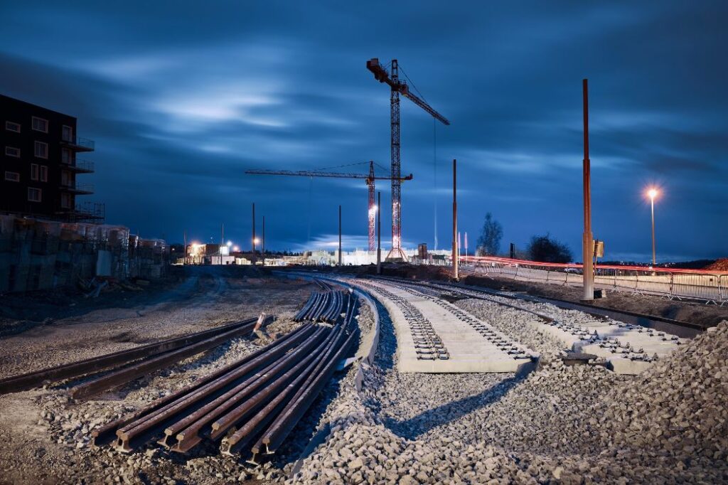 Abendliche Baustelle mit verlegten Gleisen, Signalmasten und Baugerät – Symbolbild für Eisenbahninfrastrukturprojekte